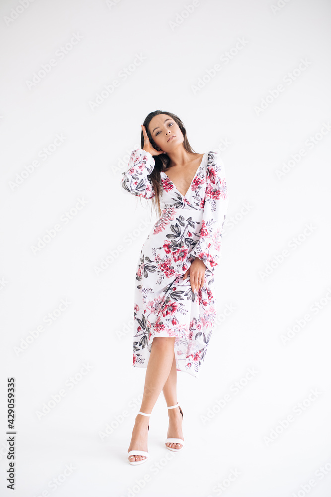 Young woman stands dressed in floral pattern dress on white background. Young woman stands dressed in floral pattern dress on white background.