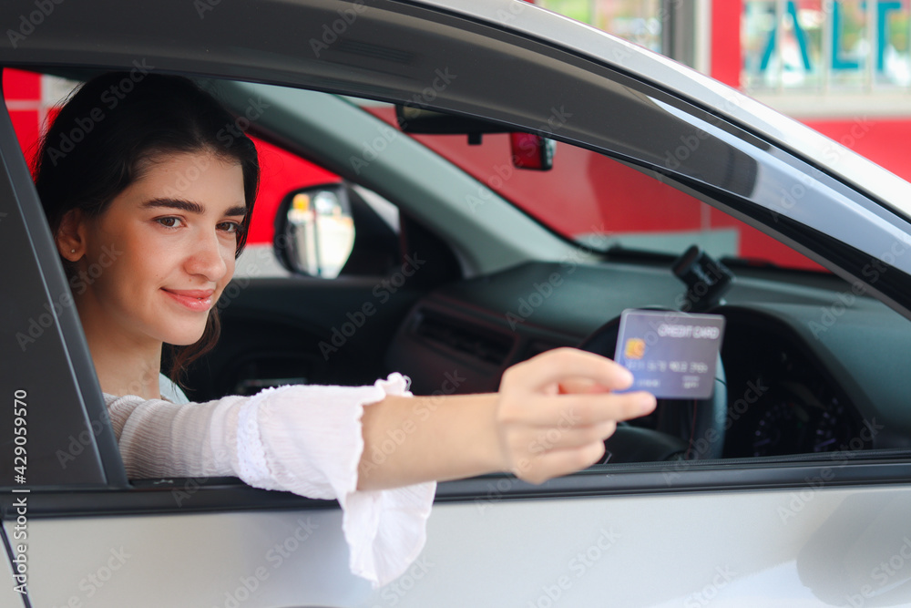 Customer woman holding credit card (mock up) for payment at gas station, young beautiful lady in car waiting for to pay with credit card.