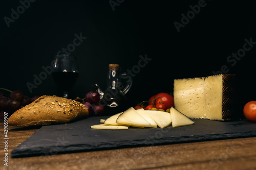 wine, cheese, bread, tomatoes on a board on a black background