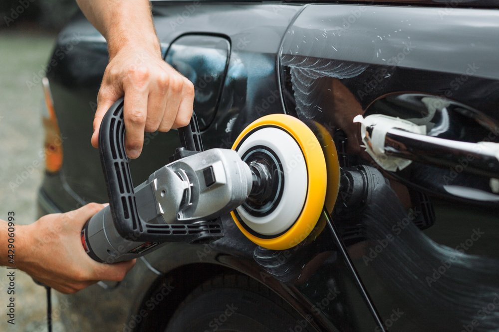 Obraz premium Polishing a used car with an electrical orbital buffer or polisher