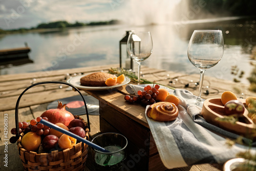 Romantic picnic by the river with panoramic backdrop. The beauty of the setting sun  fresh fruits  pastries and wine. A romantic outdoor dinner.