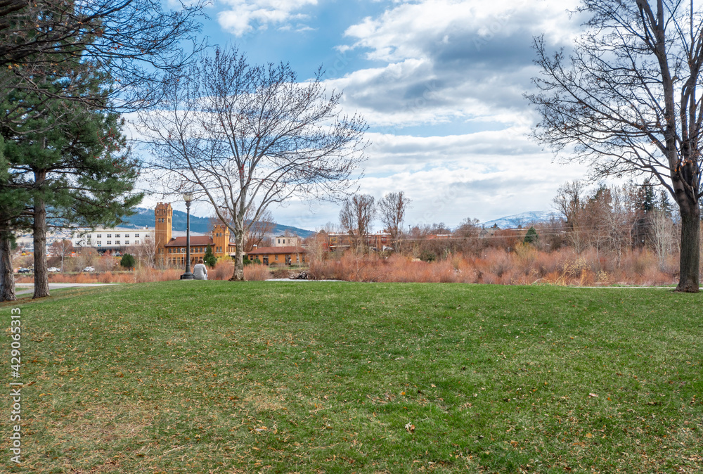 A woman relaxes at a public park along the Clark Fork River with downtown Missoula, Montana, USA seen in the distance.