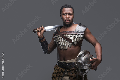 Photography Combative black gladiator holding sword on his shoulder