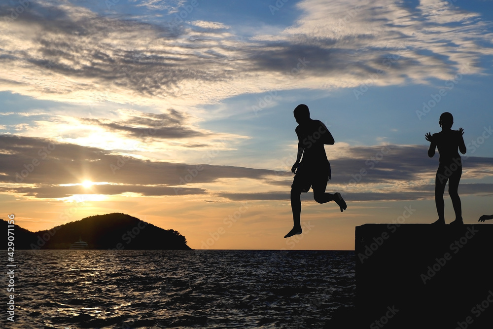Silhouettes of unrecognizable children jumping in the sea at sunset. 