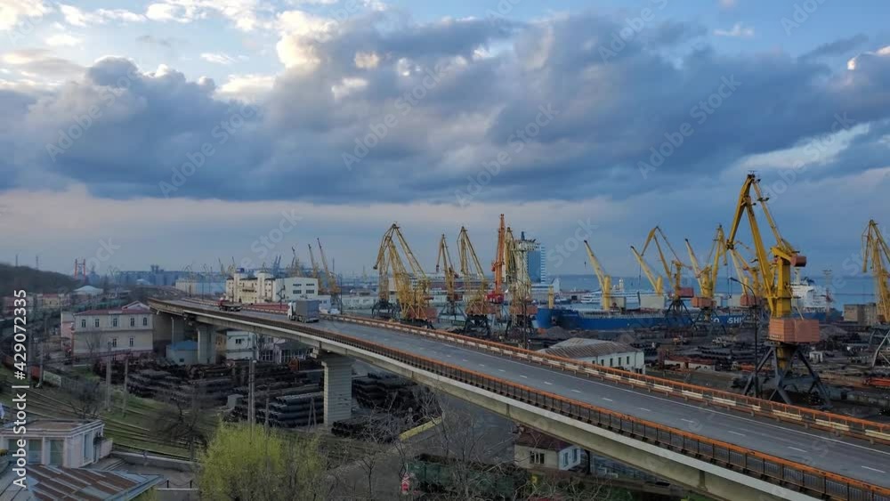 Cargro trucks drive by overpass road and cargo train passing by railway under skyway. Maritime port landscape with yellow cargo cranes at waterfront. Slow motion pan view Cargro trucks drive by overpass road and cargo train passing by railway under skyway. Maritime port landscape with yellow cargo cranes at waterfront. Slow motion pan view