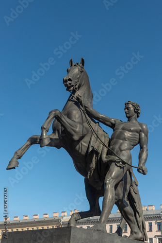 Bronze sculpture of athlete taming horse at an Anichkov bridge in St. Petersburg against the blue sky.