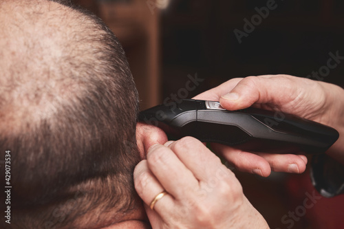 Wife cutting husbands hair at home with a haircut machine or hair clipper.