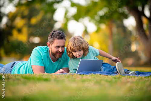 Son with father watching lesson on laptop outdoors.