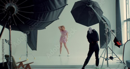 WIDE FIXED Behind the scenes of a photo shot, professional female photographer taking pictures of a fashion model in a bright studio with a lot of lights. Shot with 2x anamorphic lens photo