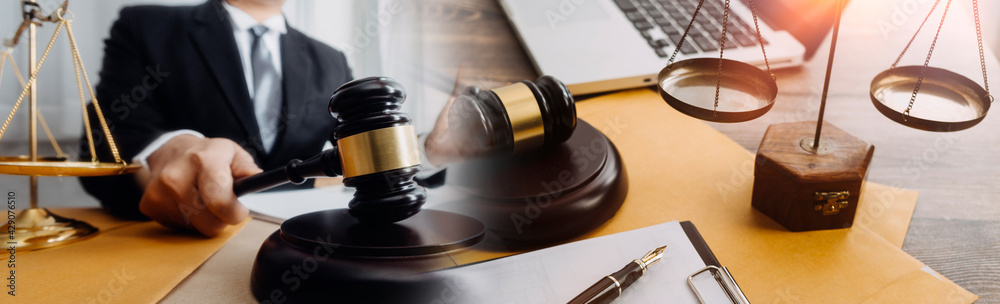 Justice and law concept.Male judge in a courtroom with the gavel, working with, computer and docking keyboard, eyeglasses, on table in morning light