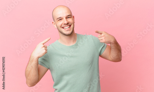 bald man smiling confidently pointing to own broad smile, positive, relaxed, satisfied attitude photo