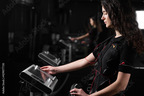 Girl in EMS suit in gym. Sport training in electrical muscle stimulation suit. photo