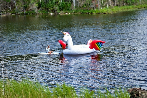 Fotografie teen paddle boarding to a huge inflatable unicorn floaty in the middle of a lake