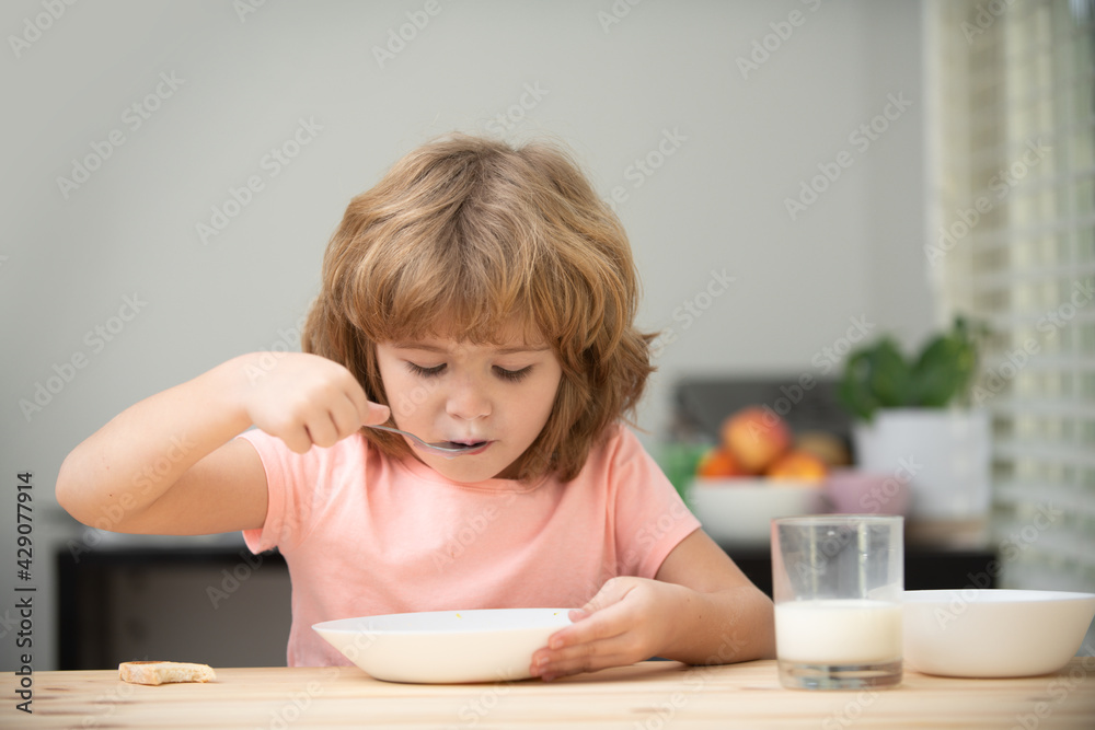 Portrait of child eating soup meal or breakfast having lunch by the table at home with spoon. Kids healthy food. Portrait of child eating soup meal or breakfast having lunch by the table at home with spoon. Kids healthy food.