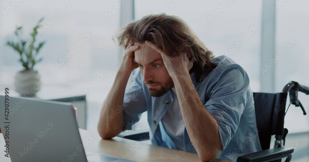 Young depressed office worker sitting by desk worry about work. Disabled invalid young man frutrating having problems at work. Young depressed office worker sitting by desk worry about work. Disabled invalid young man frutrating having problems at work.