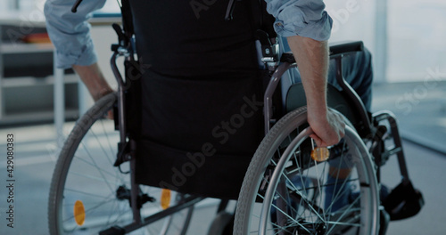 Young man in black wheelchair moving along the corporate office. Employee business person with disabilities entering office to start work.