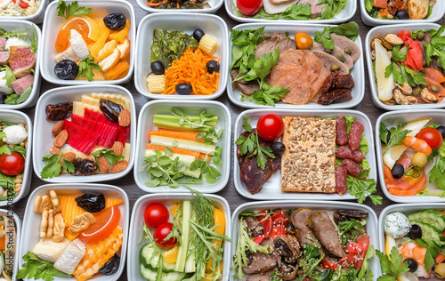 Airplane food presentation with variety of in flight meals. Flight catering. Food on airplanes. Salad bar buffet display in restaurant. Meat cuts. Hot appetizers. Close-up, a lot of food. 