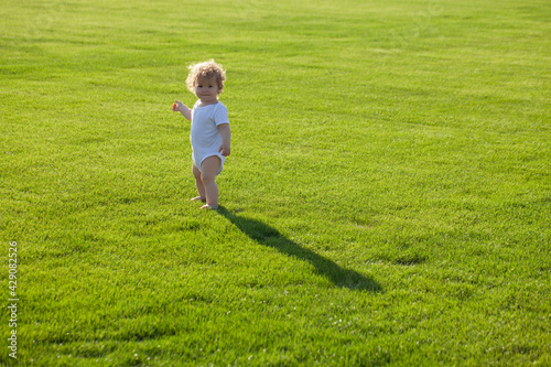 Baby standing barefoot on the green lawn.