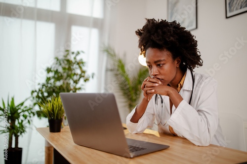 Worried black female doctor working on computer at her desk.