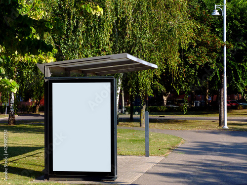 image composite of bus shelter and bus stop. blank light box. glass structure. park like urban setting. green background. empty white poster ad and blank white space for adverts. mockup base.