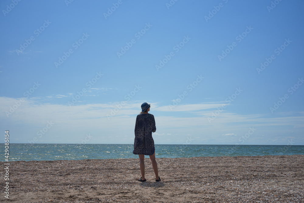 Single woman stands on the beach and enjoys the beautiful view of the sea and the wide beach