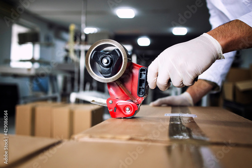 Close up view of worker's hand holding handle cutter tape machine and packing food in factory. photo