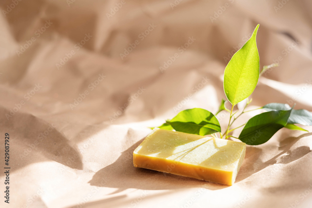 Handmade soap bar and green leaves on paper background with shadow. Concept of natural organic spa cosmetics. Herbal products. Top view, flat lay Handmade soap bar and green leaves on paper background with shadow. Concept of natural organic spa cosmetics. Herbal products. Top view, flat lay