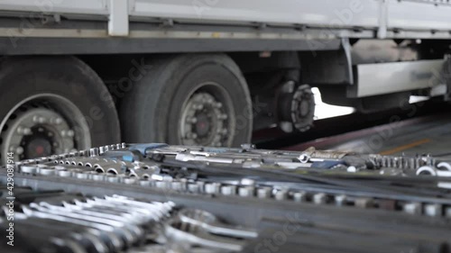A mechanic with a tool in his hands goes through the repair area along the cargo trailer. In front of the camera is a set with professional tools.