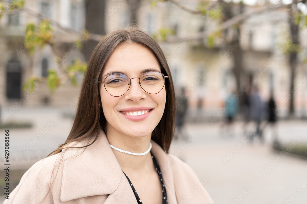 Portrait of a cheerful woman wearing glasses and smiling standing in the city park 