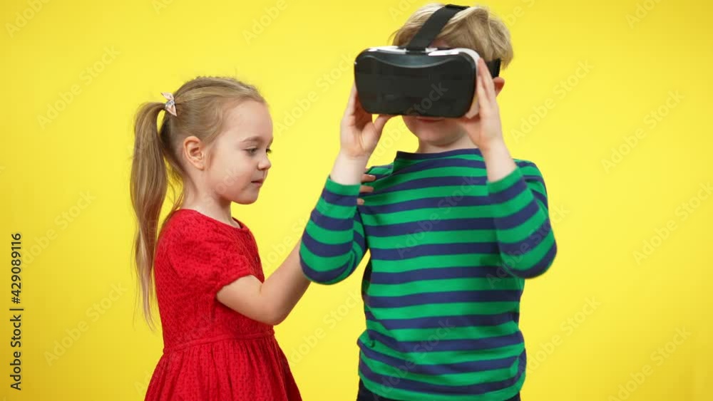 Cute Caucasian girl pulling hand of absorbed boy in VR headset. Pretty little sister distracting engrossed brother or friend gaming in augmented reality. Modern technologies and childhood Cute Caucasian girl pulling hand of absorbed boy in VR headset. Pretty little sister distracting engrossed brother or friend gaming in augmented reality. Modern technologies and childhood
