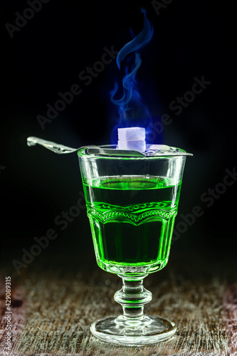 classic absinthe cup with metal spoon and sugar melting in blue flame photo