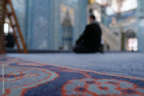 out of focus Muslim man praying in a mosque and sitting on ground while executing salah from low angle
