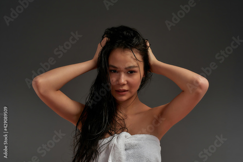 Young beautiful asian half naked woman in bath towel tousled her hair with one hand