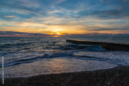 Beautiful sunset over the sea and stone pier with clouds and horizon on the beach in Sochi, Russia