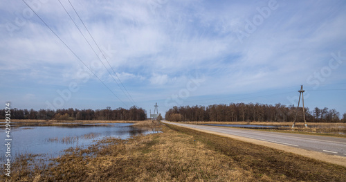 Electric transmission line support against the background of the landscape. A flooded field on the outskirts of the village. Rural landscape in early spring. High water on the outskirts of the village