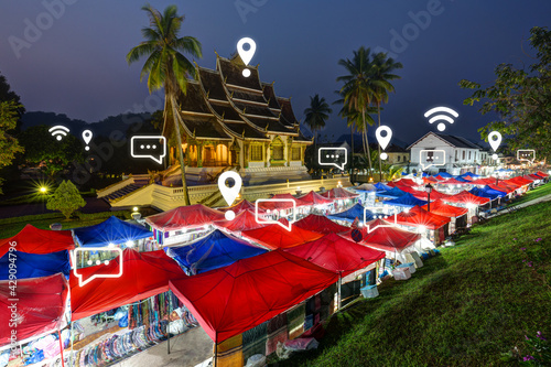 Map pin, WiFi and message icons on Luang Prabang's cityscape at dusk. Night market and Haw Pha Bang temple in Luang Prabang, Laos. Travel, wireless network connection, WiFi and messaging concept. © tuomaslehtinen