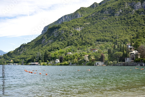 Italy Lierna, June 22 2018. Horizontal panorama of fresh lake Como surrounded by hills covered with green cedar forest