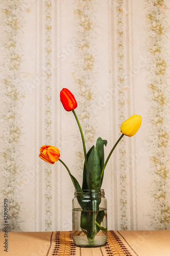 Three red and yellow tulips in the glass jar. Retro vibes. Copy space