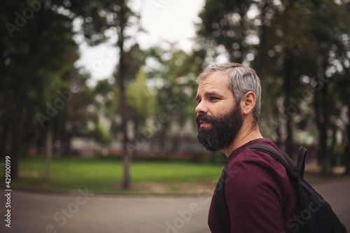 Portrait of a young bearded man walking outdoors on a city street. Middle age handsome man looking to the side and crosses the road.