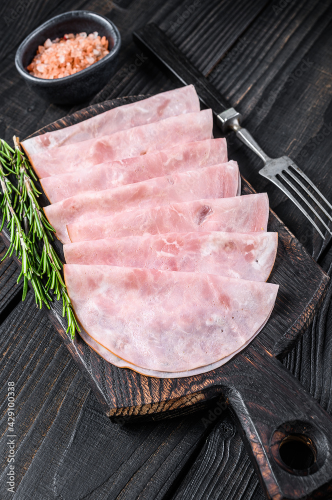 Sliced prosciutto ham on wooden cutting board. Black wooden background. Top view