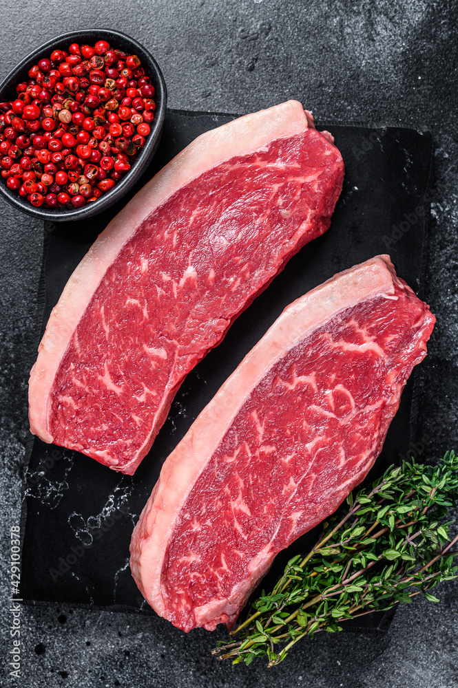 Raw cap rump steak or top sirloin beef meat steak on marble board. Black background. Top view