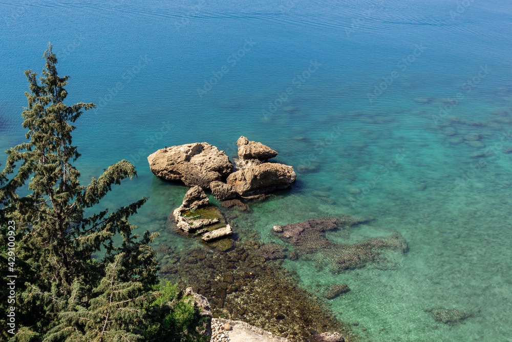 Obraz premium View of pure blue sea water, huge stones and tops of green trees.