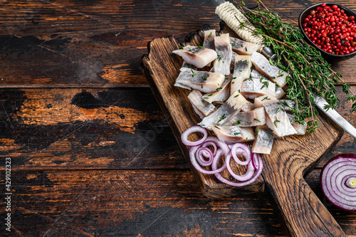 Salted herring fish sliced fillet on a wooden board with thyme. Dark wooden background. Top view. Copy space