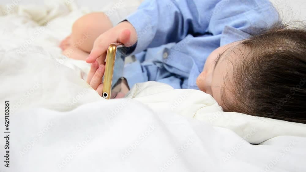Child with a phone. Phone in children's hands close-up. The child clicks on the phone screen while lying on the bed. Little girl plays on the phone while lying on the bed. Children and technology