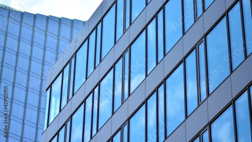 Blue sky reflection in glass facade of building. View of office building windows close up with sunrise, reflection and perspective.. Glass facade on a bright sunny day with sunbeams on the blue sky. 