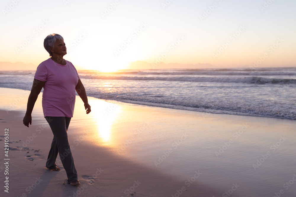 Senior african american woman walking on the beach during sunset