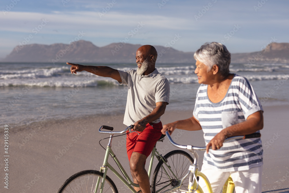 Senior african american couple with bicycles pointing towards a direction at the beach