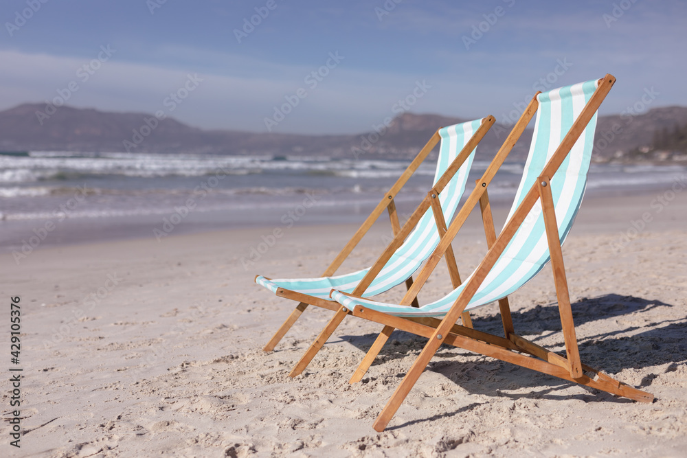 View of two deck chairs on the beach with sea waves