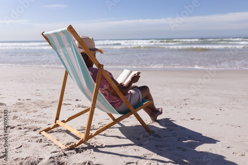 Bild auf Leinwand Senior african american woman reading a book while sitting on deck chair at the