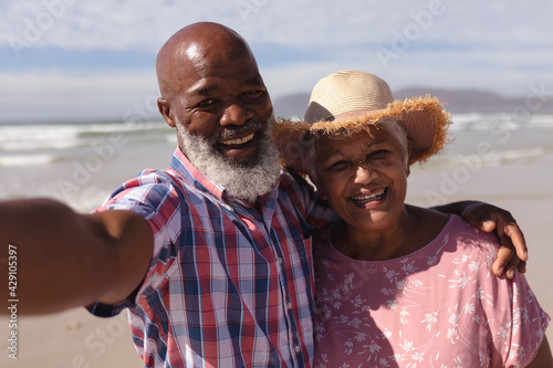 Portrait of happy senior african american couple taking a selfie at the beach